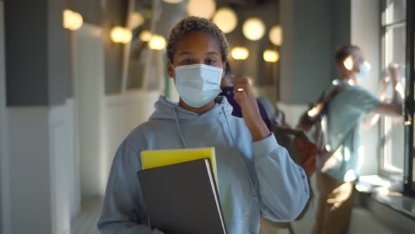 African Student Looking at Camera and Putting Off Face Mask Standing in College Corridor