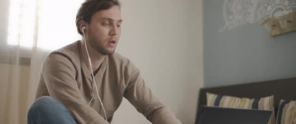 A young man speaking to someone through earphones while working on his laptop