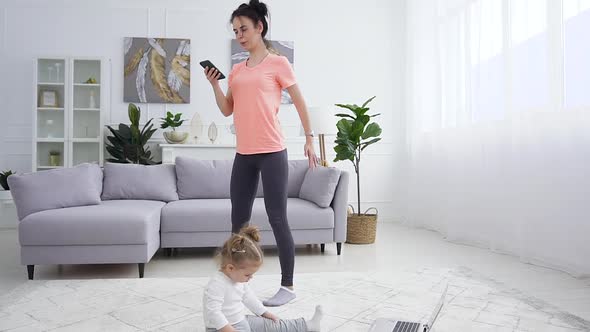 Small Girl Sitting on the Floor Near Laptop while Her Mother Doing Squat Exercises