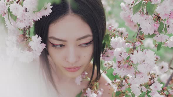 Portrait of a Beautiful Asian Girl Outdoors Against Spring Blossom Tree