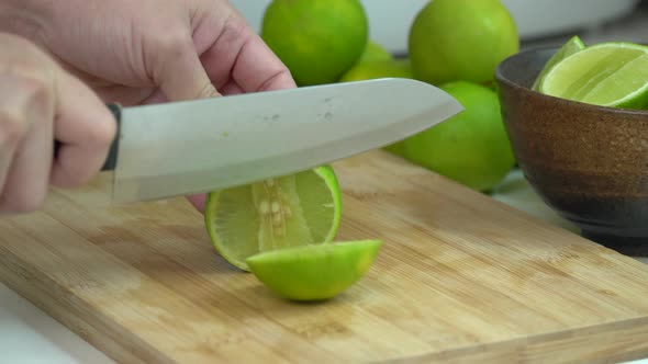 Hand Slicing fresh Lime With Knife On Wooden Board In Kitchen