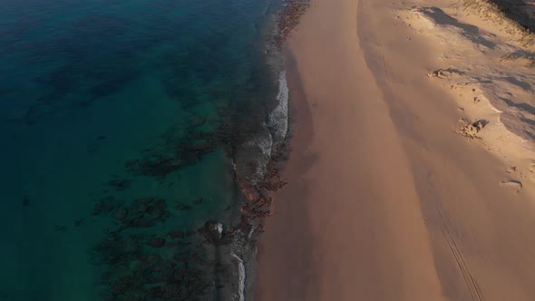Aerial tilt-up reveal over Matadouro golden beach at sunrise. Portugal