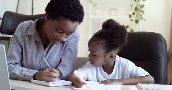 African Black Woman Mom Helping Cute Beloved Daughter Schoolgirl with Homework Sitting Together at