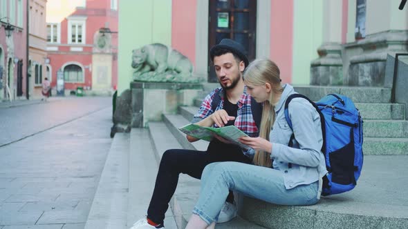 Happy Tourist Couple Sitting on Street Stairs, Checking City Map and Discussing