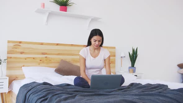 Сheerful Young Woman Working at Home Using Laptop in Bed in the Morning