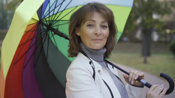 Confident Caucasian Woman Spinning Multi-colored Umbrella and Smiling. Happy Adult Female Standing