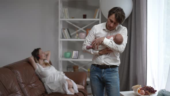 Portrait of Happy Father with Baby Son in Hands Standing in Living Room As Relaxed Mother Listening