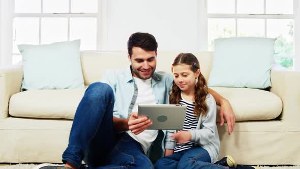 Father and daughter using digital tablet in living room