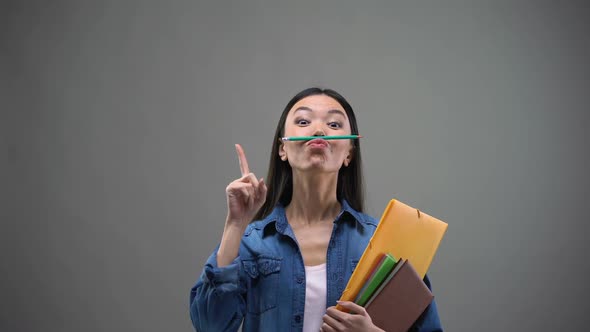 Female Student With Notebooks Having Fun Holding Pencil With Lips, Creativity