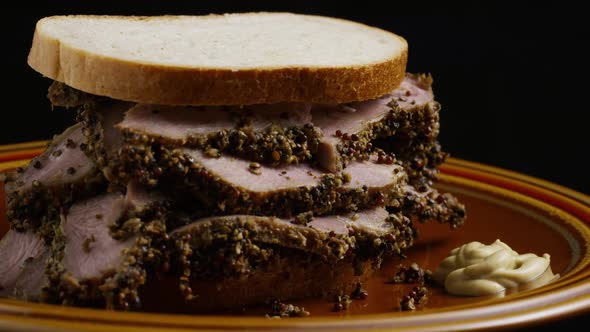 Rotating shot of delicious, premium pastrami sandwich next to a dollop of dijon mustard 