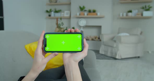 Young Woman at Home Lying on a Couch Using with Green Mock-up Screen Smartphone in Horizontal