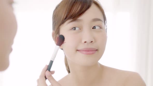 Beauty young asian woman smile with face looking mirror applying makeup with brush of cheek.