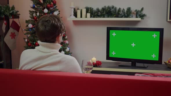 A guy wtith a glass of wine watching Green Screen Mockup TV in a Chrismas decorated living room.