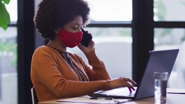 Mixed race businesswoman wearing mask sitting using a laptop in office