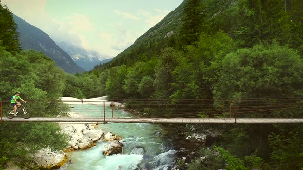 Aerial view of a woman crossing a wooden bridge on a mountain bicycle.