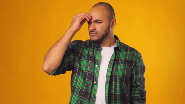 Pensive African American Man Touching His Forehead and Thinking Against Yellow Background