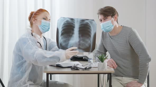 Concentrated Caucasian Woman and Man in Covid19 Face Masks Talking Pointing at Lungs Xray