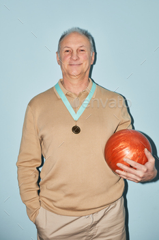 olding bowling ball while standing against blue background, shot with flash