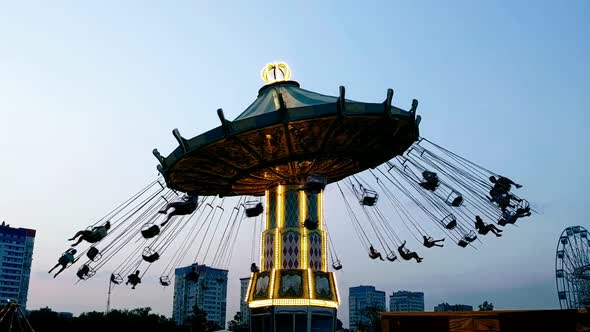 Carousel with dark silhouettes people spinning quickly against the background of the evening sky