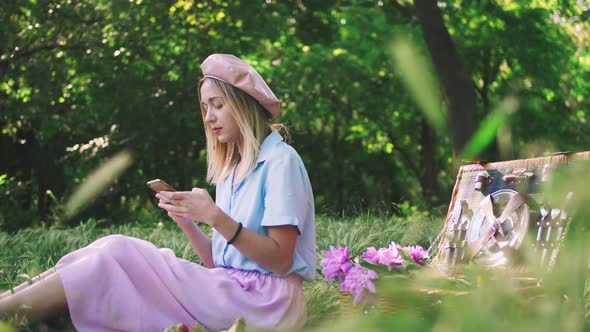 Young Stylish Woman Using Her Cell Phone Outdoor in the Park on Picnic