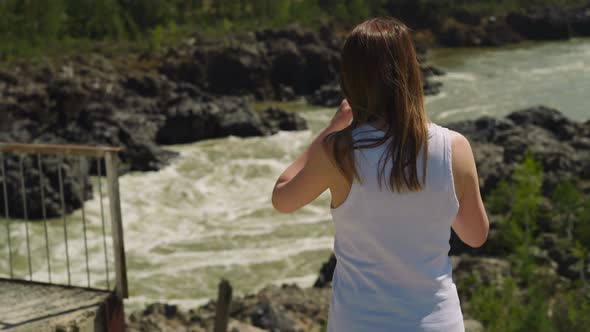 Woman Adjusts Hair Standing on Rocky Bank of Mountain River