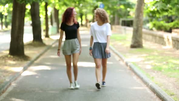 Two beautiful girls walking and laughing at park