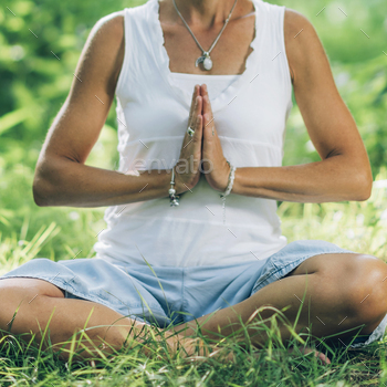 ing attunement and centering through meditation. Sitting on the ground with crossed legs, hands in a prayer position, and eyes closed, feeling balanced and centered