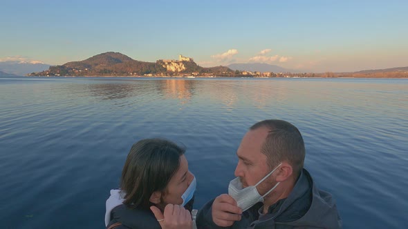 Couple in love takes off masks due to covid and kiss with lake and castle in background at sunset