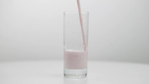 Pink Healthful Fruit Yogurt Pouring in Transparent Glass Closeup