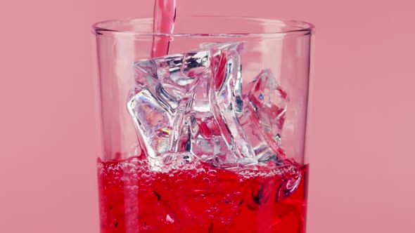 Pouring Red Soft Drink Into a Glass with Ice Cubes