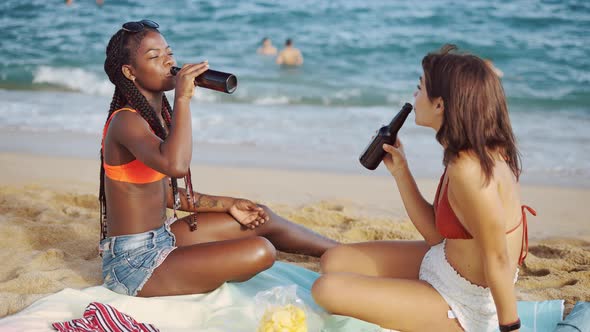 Best Friends Sitting on Beach Drinking From Bottles