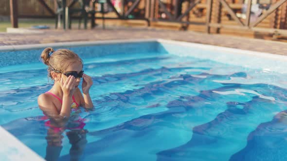 A Girl in a Bright Swimsuit with Swimming Goggles Dives Into a Pool with Clear Transparent Water