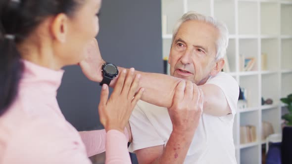 Video of happy biracial female physiotherapist exercising with caucasian senior man