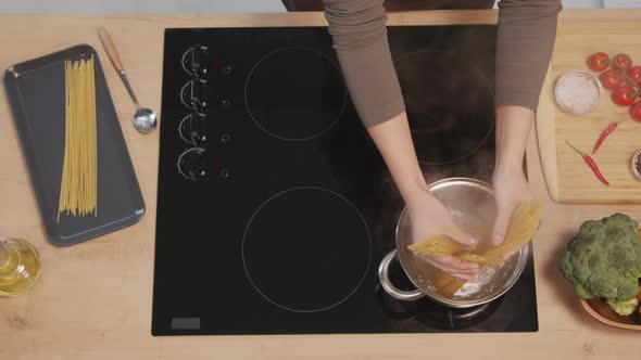 Female Hands Putting Spaghetti in Pot with Boiling Water