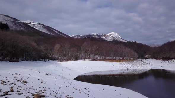 Beautiful lake surrounded by snow, forest in the background, sky full of clouds. Pantà de Santa Fe,