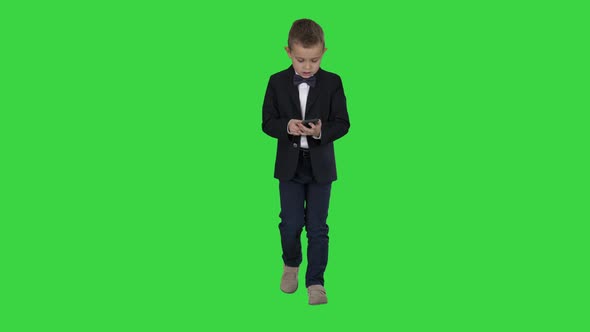 Small Boy in Costume Walking and Using Smartphone on a Green Screen