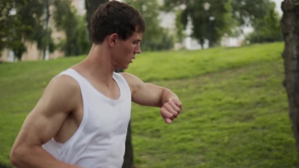 A muscular guy is running  while using his fitness tracker
