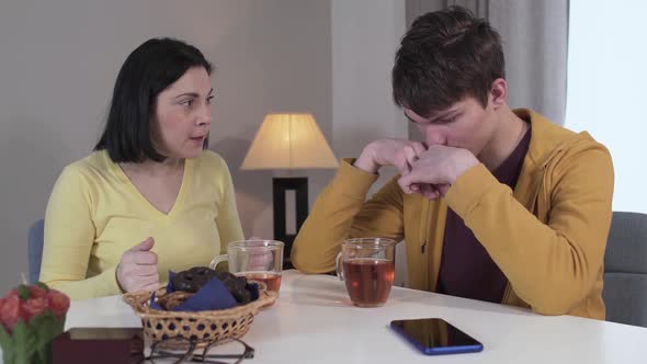 Upset Teenage Caucasian Boy Closing Face with Hands As His Angry Mother Scolding Him. Stressed