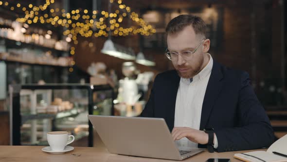 Businessman Sitting at the Cafe and Typing at the Laptop