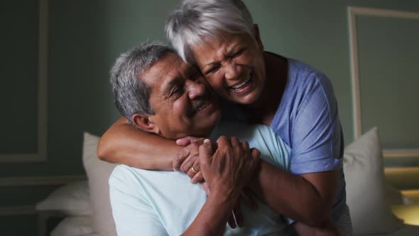 Senior mixed race couple embracing and laughing in bedroom
