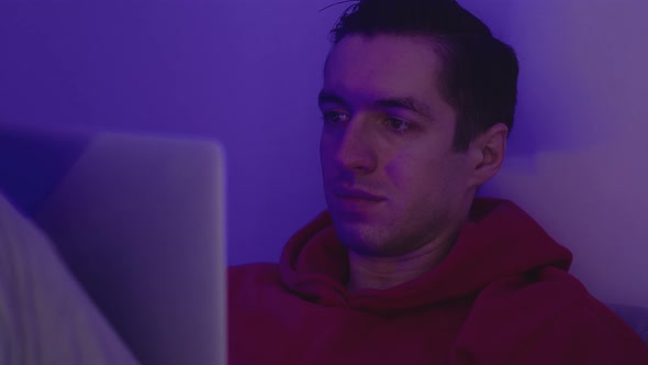 Young Man Using Laptop Computer While Lying in the Bedroom at Home at Nighttime