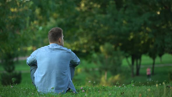 Back View of Man Sitting on Grass at Park, Enjoying Weekend in Loneliness