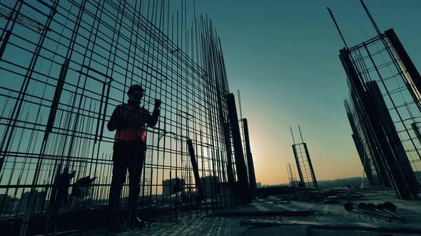 Male Builder Knits Metal Carcass on Sunset Background.