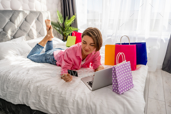 pretty happy woman lying on bed at home shoppping online