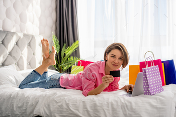 pretty happy woman lying on bed at home shoppping online