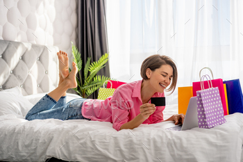 pretty happy woman lying on bed at home shoppping online