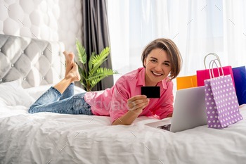 pretty happy woman lying on bed at home shoppping online