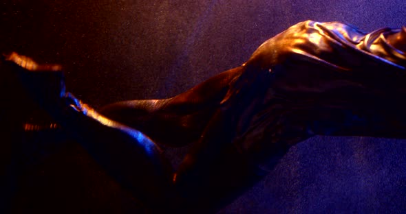 Close-up Women Legs in Silver Tights Swim Underwater in a Tnmnot in Neon Light