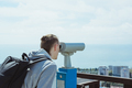 young hipster tourist man looking through metal coin operated binoculars on sea, sky and city - PhotoDune Item for Sale