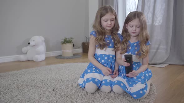 Portrait of Charming Brunette Caucasian Twin Sisters Switching Channels with Remote Control, Joyful